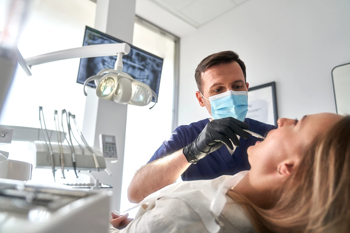 Dentista realizando procedimento de anestesia em paciente em consultório odontológico, ambiente moderno e bem iluminado com equipamento odontológico ao fundo.
