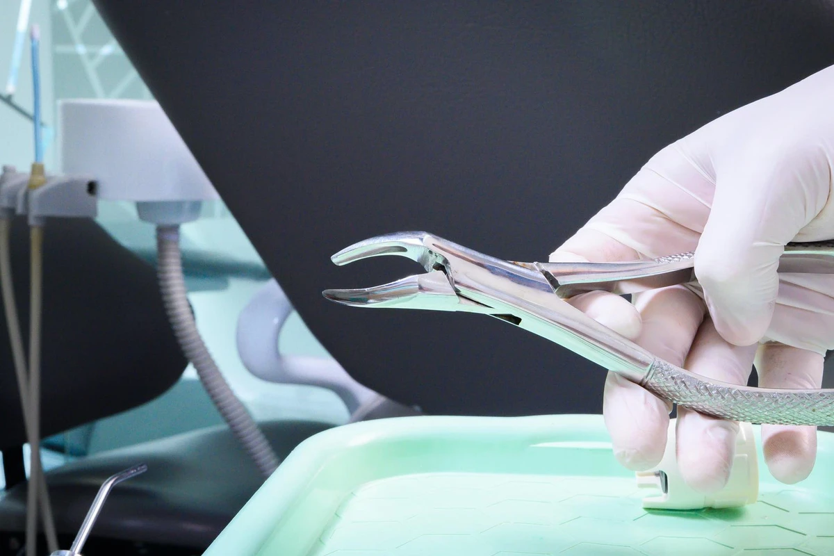 Profissional de odontologia segurando instrumento cirúrgico para extração de dente em ambiente clínico.
