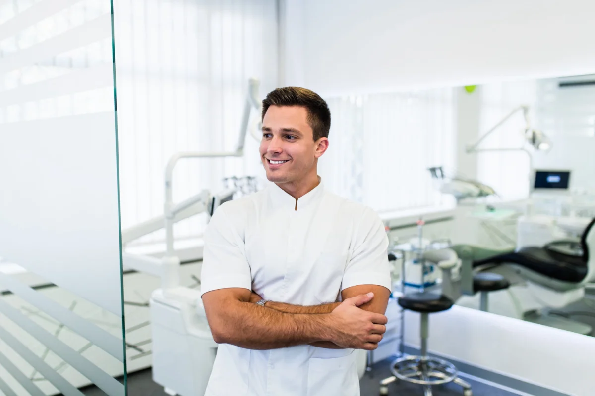 Dentista sorridente em consultório odontológico moderno com equipamentos ao fundo